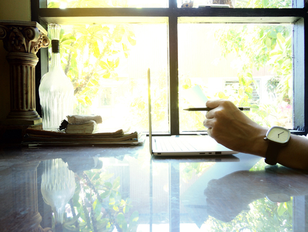 Businesses happen everywhere, just have inspiration. The picture of white laptop with Male hand on wooden table near the window at home office. selective focusの写真素材