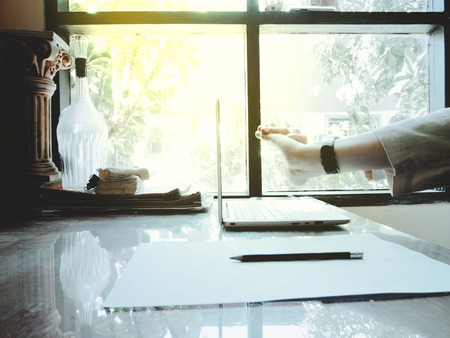 Businesses happen everywhere, just have inspiration. The picture of white laptop with Male hand on wooden table near the window at home office. selective focusの写真素材
