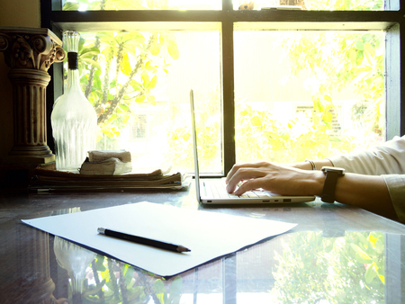 Businesses happen everywhere, just have inspiration. The picture of white laptop with Male hand on wooden table near the window at home office. selective focusの写真素材