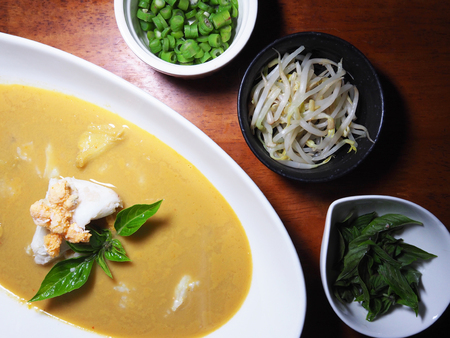 Top view picture of Thai curry crab on white dish above wooden table served with boiled Thai basil, boiled long bean sliced and boiled Sprout.の写真素材