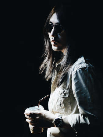 Portrait of white Asian men long hair hold coffee cup, dress casual style on black background. Light and shadow portrait styleの写真素材