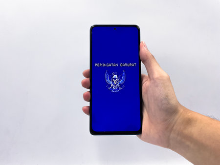 Peringatan Darurat viral Indonesian national politic movement against the government. Hand holding phone with blue retro vintage screen and Indonesian Garuda logoの写真素材