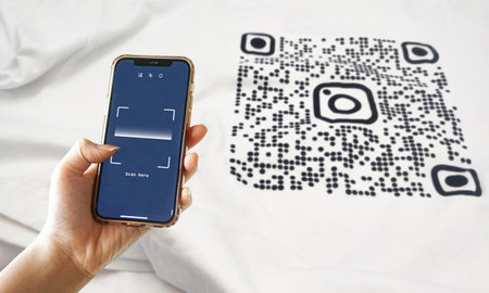 Hand holding smartphone ready to scan QR code printed on white shirt. Convenient digital technology conceptの写真素材