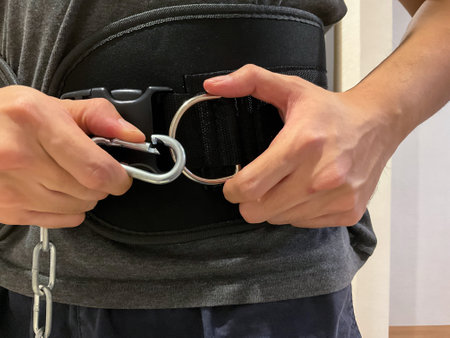 Man adjusting chains on weightlifting belt, close up view. Preparing for gym workout, no face shown on cameraの写真素材