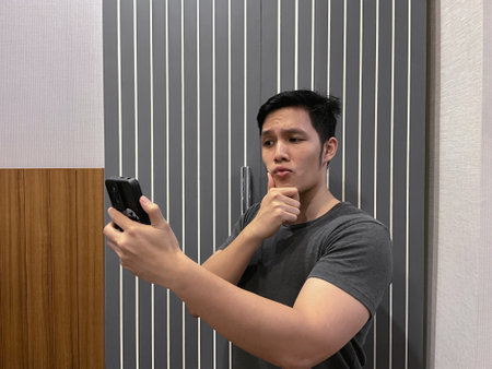 Handsome young man taking selfie using phone camera while posing, hand on chin.の写真素材