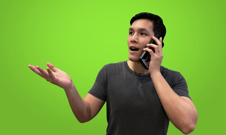 Person talking on smartphone wearing casual outfit, explaining with hand gesture, isolated on bright greenscreen backdrop.の写真素材