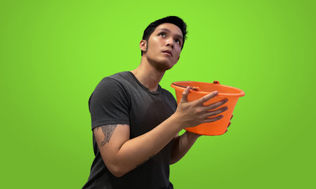 Tattooed person holding orange bucket, Wearing dark gray t-shirt isolated on bright green screen backdropの写真素材