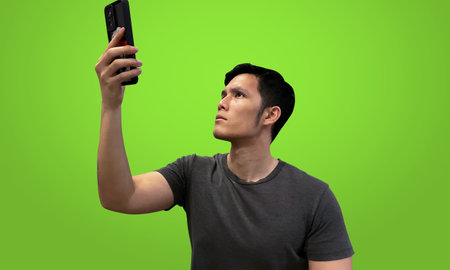 Man raising phone up to search for signal, isolated on green screen backdrop. Bad network concept.の写真素材
