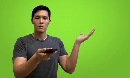 Confused man holding tv remote control, one hand raised, isolated on green screen background.の写真素材