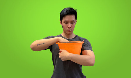Tattooed man reaching into orange bucket looking for something. Casual wear, isolated on green screen background.の写真素材