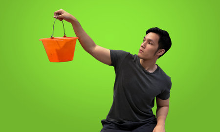 Person holding orange bucket, Wearing dark gray t-shirt isolated on bright green screen backdropの写真素材