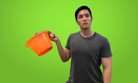 Person holding orange bucket with blank expression, Wearing dark gray t-shirt isolated on bright green screen backdropの写真素材