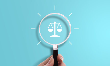 Hand holding magnifying glass with scale icon, symbol of justice, law, and legal system.の写真素材