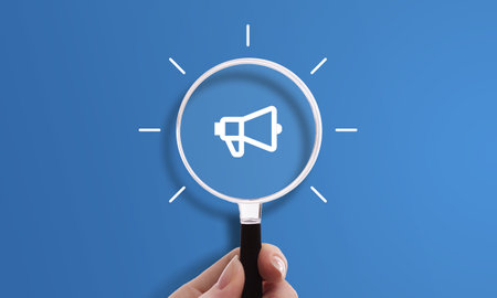Hand holding magnifying glass with megaphone icon, symbol of marketing and promotion.の写真素材