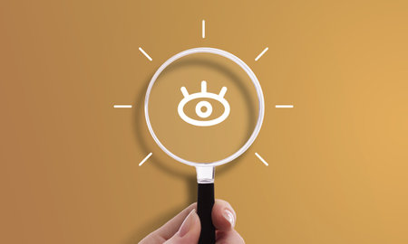 Hand holding magnifying glass with eye icon, symbol of vision, insight, and market researchの写真素材