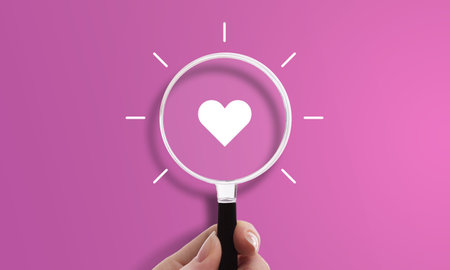 Hand holding magnifying glass with heart icon, symbol of love and romanceの写真素材