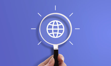 Hand holding magnifying glass with web icon, symbol of internet, international business, and global networkの写真素材