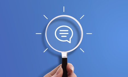 Hand holding magnifying glass with bubble chat icon, symbol of customer service, communication, and conversationの写真素材
