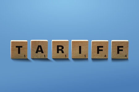 Wooden tile with letters spelling the word TARIFF isolated on blue background. Import tax concept.の写真素材
