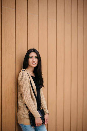 Stylish woman smiling stands near a wooden wall.の写真素材