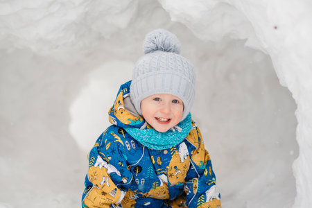 cute young boy child is playing outside in igloo fort tunnel he dug in pile of snow on winter day.の写真素材