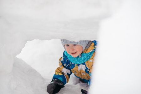 cute young boy child is playing outside in igloo fort tunnel he dug in pile of snow on winter day.の写真素材