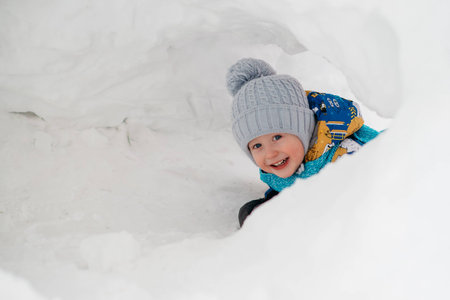 cute young boy child is playing outside in igloo fort tunnel he dug in pile of snow on winter day.の写真素材