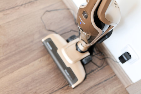 OSTRAVA, CZECH REPUBLIC - APRIL 16, 2019:  Charging the brown portable cordless Sencor vacuum cleaner on a wooden floor for cleaning a household with a sofa in the backgroundのeditorial素材