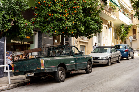 ATHENS, GREECE - FEBRUARY 4, 2019: An orange tree with a lot of free citrus fruits on a streets of Athens city and cars parked below it.のeditorial素材
