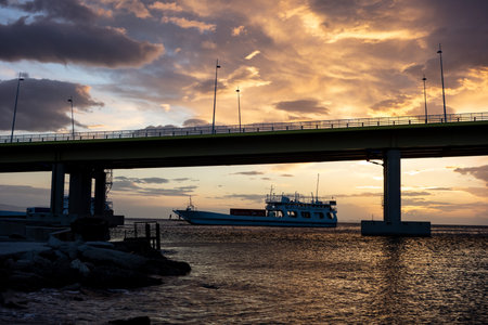 PATRAS, GREECE - FEBRUARY 6, 2019: The famous Rio-Antirrio multi-suspension bridge (Charilaos Trikoupis Bridge) during the beautiful sunset with a ferry ship in the backgroundのeditorial素材