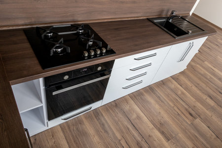 A modern gas cooker with ceramic hob, electric oven and a dark brown wooden kitchen with wash-basin...