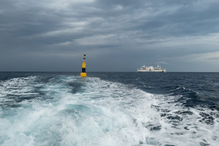 GOZO, MALTA - OCTOBER 29, 2019: The dangerous storm is coming with dark grey cloudy sky, yellow buoy and a white ferry of Gozo Channel Line company connecting Maltese islands in the backgroundのeditorial素材