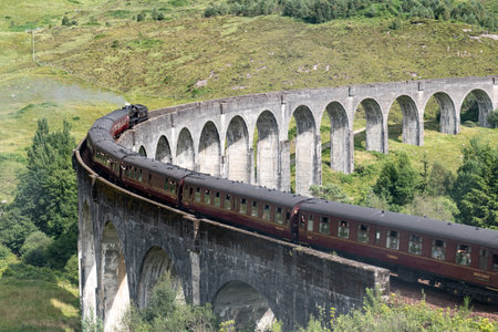 Famous Glenfinnan Viaduct in Scotland with a historic steam train and tourists with slight motion blur effectの写真素材