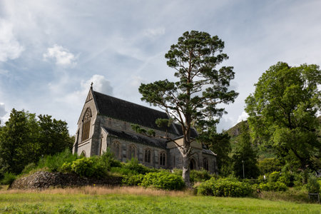 Ancient Saint Mary & Saint Finnan Catholic Church on a hill with a tree in Glenfinnan, Scotland, UKの写真素材