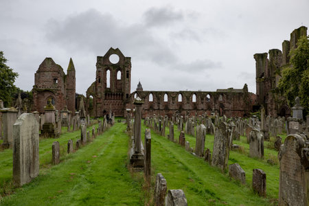 ARBROATH, SCOTLAND - AUGUST 11, 2019: Cemetery, gravestones and red brick ruins of medieval Arbroath Abbey and courtyard in Scotland in cloudy weatherのeditorial素材