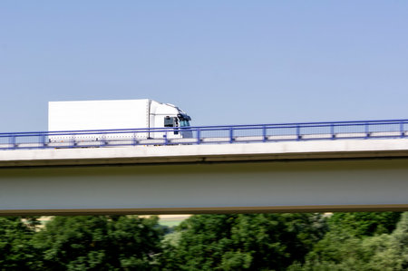 Fast driving white small truck on a highway bridgeの写真素材