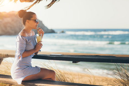 Pretty woman in summer dress drinking cocktail on beachの写真素材