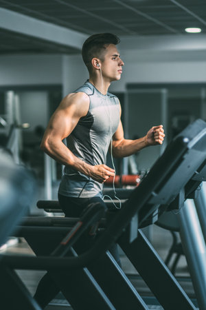 Young man in sportswear running on treadmill at gymの写真素材