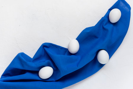 White eggs lie on a blue cloth. White background, horizontal orientation, copy space, top view.の写真素材