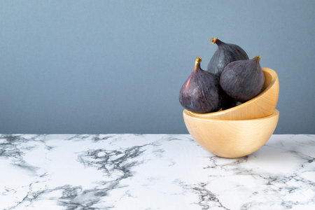 Figs lying in a wooden dish that stands on a marble countertop. Gray background, horizontal orientation, copy space.の写真素材