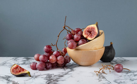 Still life with red grapes and cut figs lying in a wooden bowl. Marble table, gray background, horizontal orientation.の写真素材