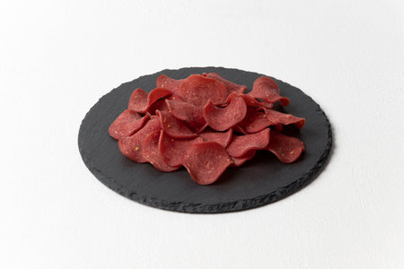 Beer appetizer meat chips on a round black slate board. Horizontal orientation, white textured background, close-up.の写真素材
