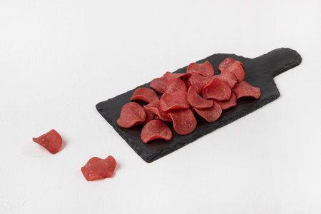 Appetizer for beer. Smoked pork chips lying on a black slate board. There are two slices next to it. Horizontal orientation, white textured background.の写真素材