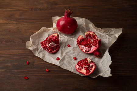 Pieces of ripe pomegranate lie on parchment paper. Wooden background, horizontal orientation, close-up, top view.の写真素材