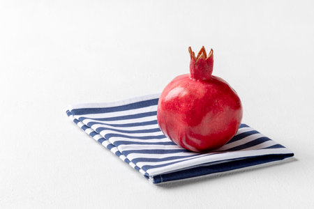 Pomegranate lies on a folded striped towel. White textured background, horizontal orientation, copy space.の写真素材
