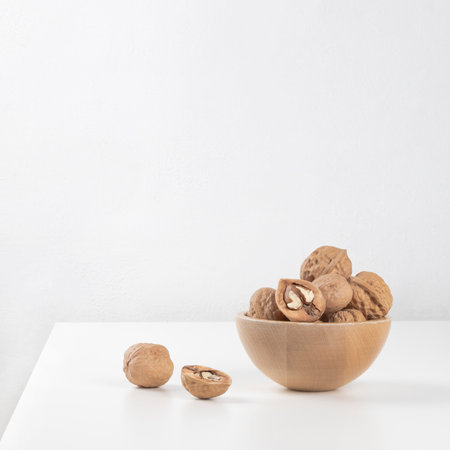 A wooden bowl with unpeeled walnuts stands on a white table.の写真素材