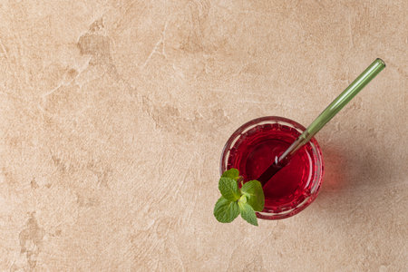 Top view of karkade tea (hibiscus) poured into a glass with a green glass tube and mint leaves. Horizontal orientation, copy space, beige textured background.の写真素材