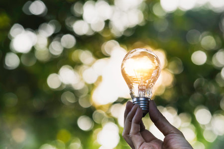 Hand holding light bulb in nature on green background for energy concept.の写真素材