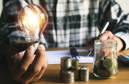 Business man holding light bulb and some coins on table writing  saving bank and account for his money all in finance accounting concept.の写真素材