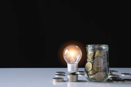 Coins and light bulb put on the table for saving money,energy concept in dark background.の写真素材